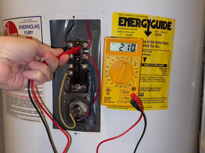 Repairman testing voltage at an electric water heater thermostat with a multimeter